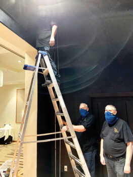 Left to right: Frank Calsbeek and his son, Frankie, assist Joey Mendoza (on ladder) with hanging the main curtain. (Photo by Shawne Cryderman)