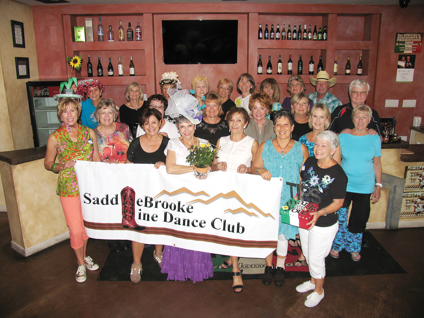 Charli Jackson (center), the decorated hat winner, wearing her creation and holding her prize of a potted yellow rose and trellis amongst the other members of the SaddleBrooke Line Dance Club.
