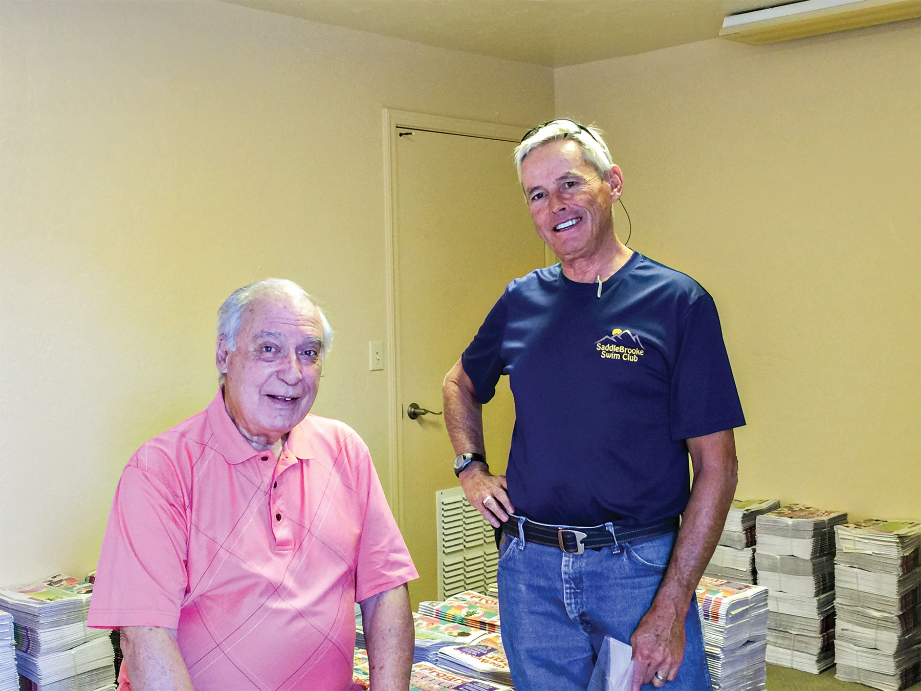 Ed Betanzos (left) and Jeff Eighmy rest after bundling the October issue of the SaddleBrooke Progress; photo by Bob Lamb. Monthly delivery of the Progress is a service project of the SaddleBrooke CycleMasters. About 5,000 newspapers are received monthly from the printer. Ed coordinates scheduling of delivery people. Jeff separates the papers into bundles by delivery route, which are neighborhood units. Later, 30 persons will arrive here to collect papers for their assigned routes. The delivery people will devote one or two hours each month