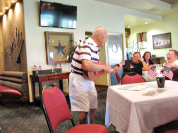 Ron Barker leads happy Unit 49 residents in a rousing rendition of our unit 49 song Nothin’ Could be Finer than to be a 49er during the annual Memorial Day event; photo by Dave Corrigan.