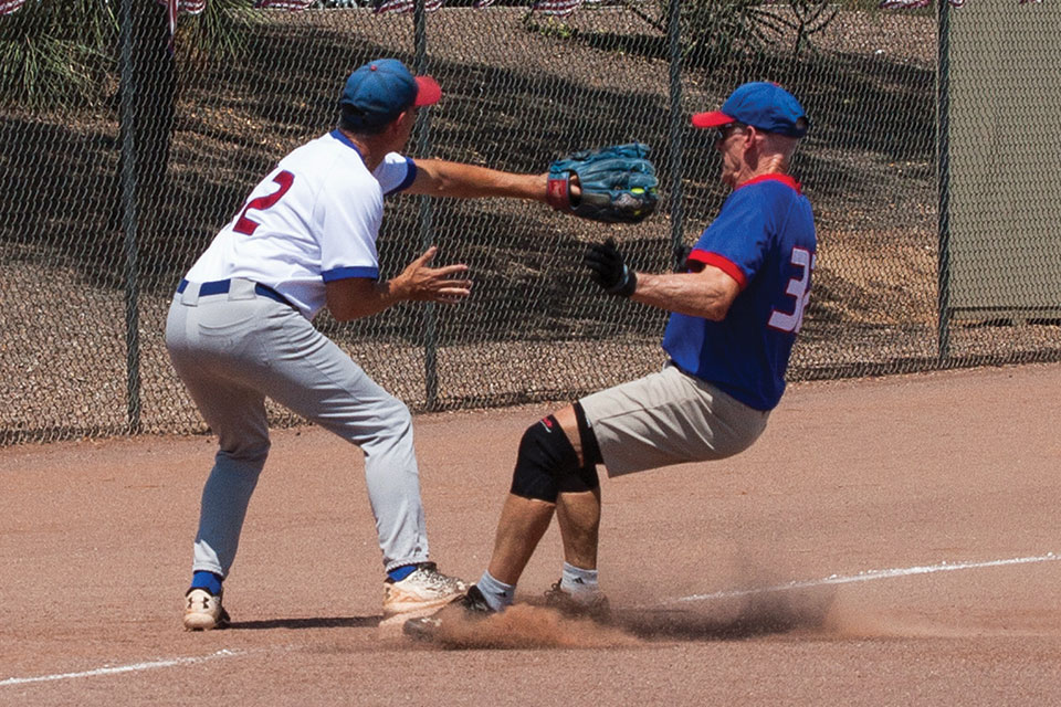 Competitive: Harold Weinenger reaches to tag runner Don Jones as he stirs up the dust at third base; photo by Dennis Purcell