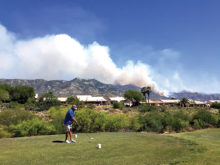Golfers teeing off and playing with the smoke clouds and fire in the background (Photo by Fred Pilster)