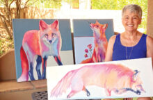 Rose Collins holds an in-progress work in her newest series. Behind her are two more paintings in this series, Foxy Lady (left) and Peaches meets Buzz. (Photo by LaVerne Kyriss)