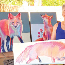Rose Collins holds an in-progress work in her newest series. Behind her are two more paintings in this series, Foxy Lady (left) and Peaches meets Buzz. (Photo by LaVerne Kyriss)