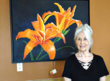 Vivian Sathre shows off “Double Lilies,” one of her large floral paintings done in an acrylic medium. (Photo by LaVerne Kyriss)