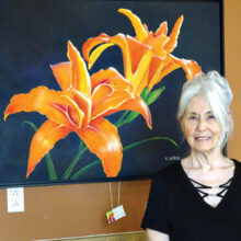 Vivian Sathre shows off “Double Lilies,” one of her large floral paintings done in an acrylic medium. (Photo by LaVerne Kyriss)